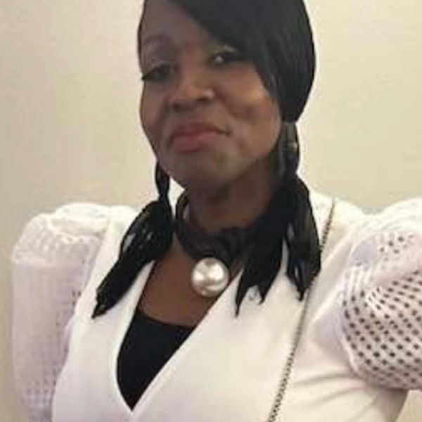 Woman in white top with pearl necklace and braided hair.