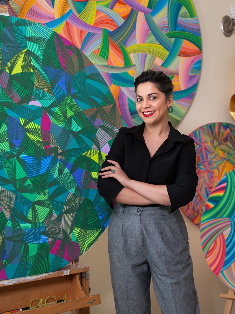 Artist posing with vibrant abstract circular paintings in the background.