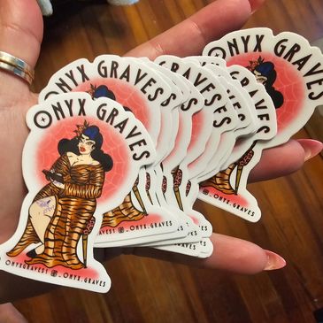Hand holding multiple Onyx Graves stickers featuring a tattooed woman in a tiger-striped dress.