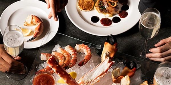 Seafood platter with crab legs, shrimp, sauces, and drinks on a dark table.