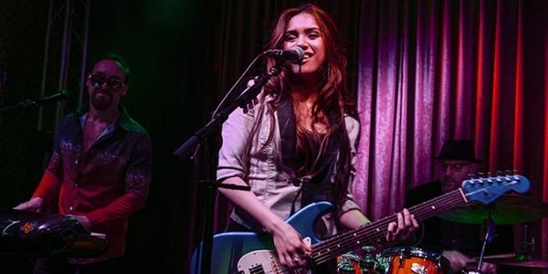 A woman singing and playing electric guitar in a live band.