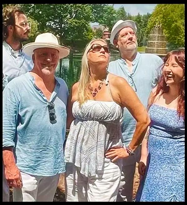 Group of five adults posing outdoors, dressed in light summer clothing.