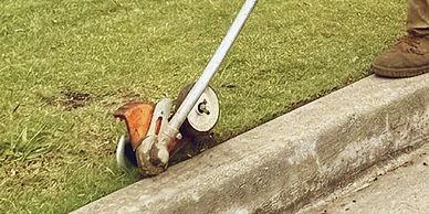 A person trims grass along a curb with a string trimmer.