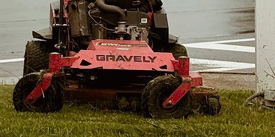 Red Gravely lawn mower cutting grass near a white building.