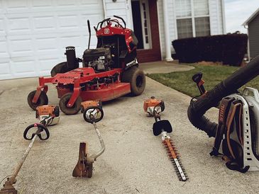 Lawn maintenance equipment arranged on a driveway beside a red riding mower.