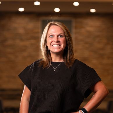 Smiling woman in black top with a brick wall background.