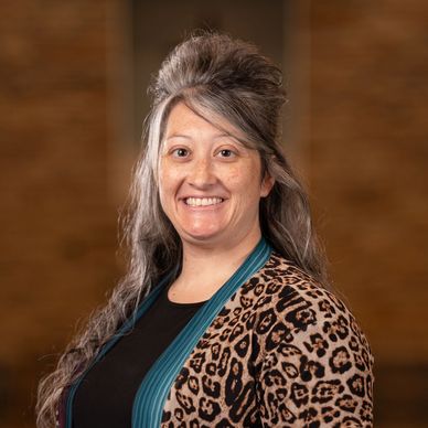Smiling woman with long gray hair and leopard print cardigan.