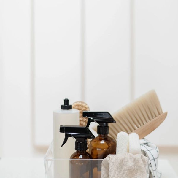 Cleaning supplies organized in a clear plastic container on a white countertop.