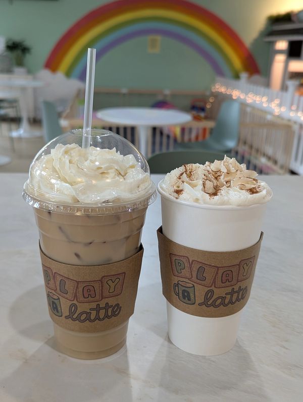 Two whipped cream topped lattes on a table with a rainbow mural in the background.