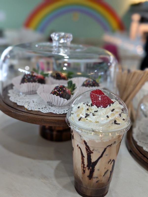 Chocolate drink topped with whipped cream and strawberry, with chocolate-covered strawberries in background.
