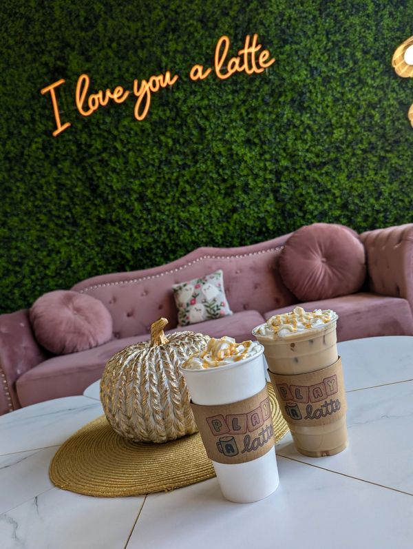 Two caramel-topped lattes on a table with a cozy couch and neon sign.