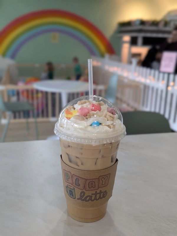 Iced latte with whipped cream and colorful cereal toppings at a playful café.
