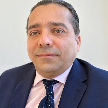 Professional man in a navy suit and polka dot tie against a plain background.