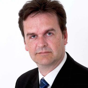 Professional middle-aged man in a black suit and blue tie against a white background.