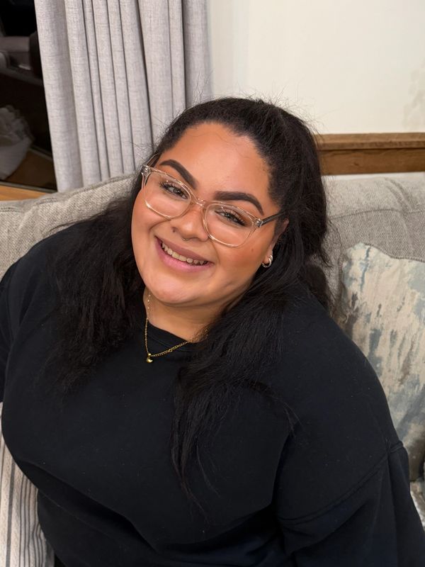 Smiling woman with glasses and black top sitting on a couch.