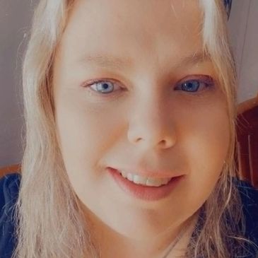 Close-up of a smiling woman with blonde hair and blue eyes.
