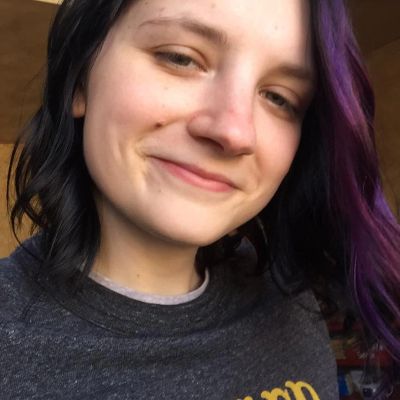 Young woman with black and purple hair smiling gently.