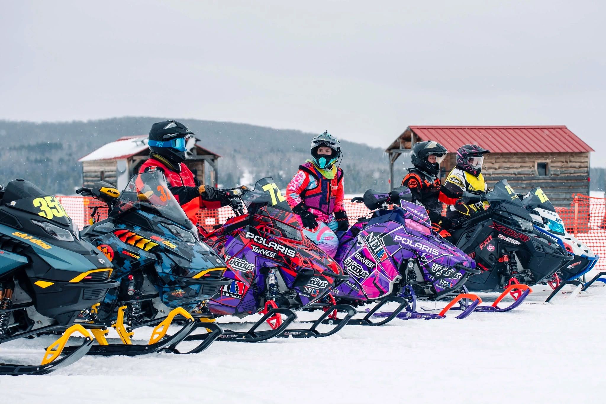 Group of snowmobilers lined up in winter gear on snowy terrain.
