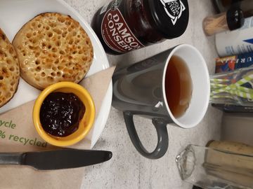 Breakfast treats ready for serving to the customer. A mug of hot black Keemun tea, and a plate with two hot buttered toasted crumpets served with Welsh Damson jam. 