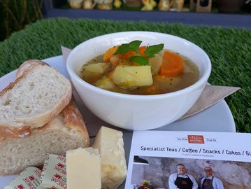 A steaming bowl of hot vegetable Cawl, served with a rustic bread roll and Welsh butter portions, and a wedge of cheddar cheese. Cawl is a traditional Welsh rustic soup.