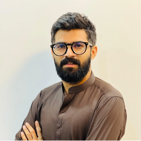 Man with glasses and beard wearing a brown traditional outfit.