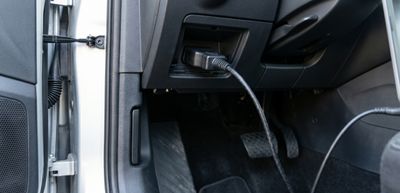 Diagnostic cable plugged into a car's OBD-II port under the dashboard.