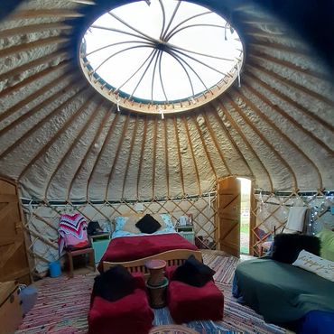 Inside spacious yurt showing seating, table and cosy living space at Sunny Hill Campsite