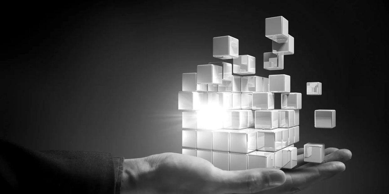 Hand holding a glowing, fragmented cube made of smaller cubes in a dark setting.