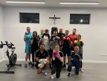 A group of people in boxing gloves posing in a gym with a punching bag.