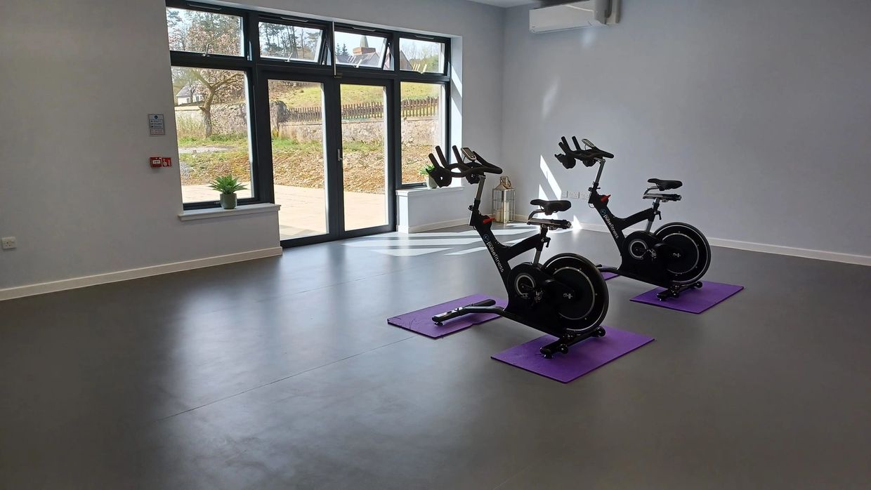 Two stationary bikes on purple mats in a bright, minimalist fitness room.