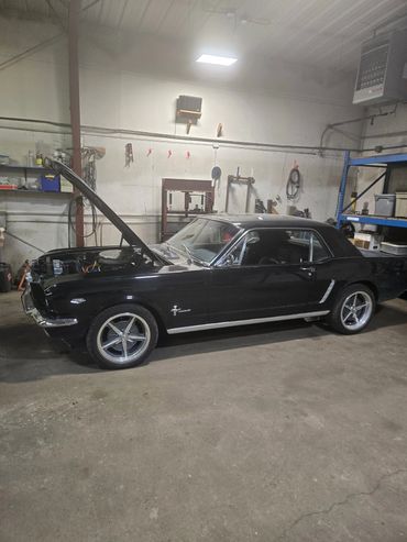 Black classic Ford Mustang with open hood in a garage.
