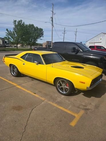 Bright yellow classic muscle car parked in a lot beside a black truck.