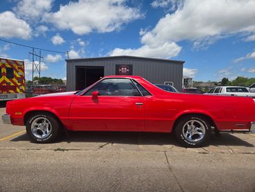 Bright red classic car with shiny chrome wheels parked outside a garage.
