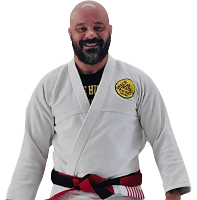 Smiling man in a white Brazilian Jiu-Jitsu gi with a black and red belt.
