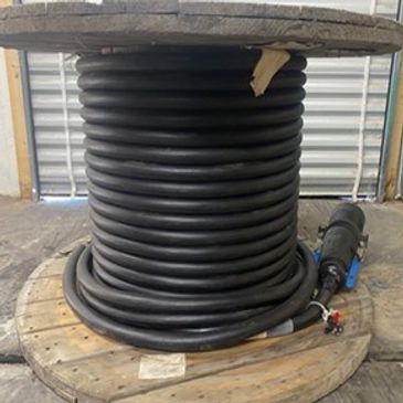 Large black cable coiled on a wooden spool inside an industrial space.