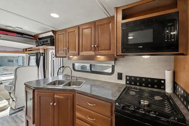Professional photograph presenting the stove, microwave, and sink in an RV listed for sale in N. TX.