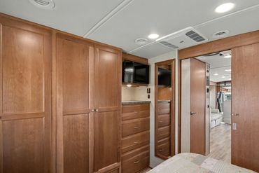 Photo illustrating the built-in closets, drawers, and TV in the master sleeping area of an RV.
