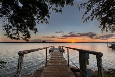 Photograph of sunset over the lake with walkway leading to private dock behind a home in north TX