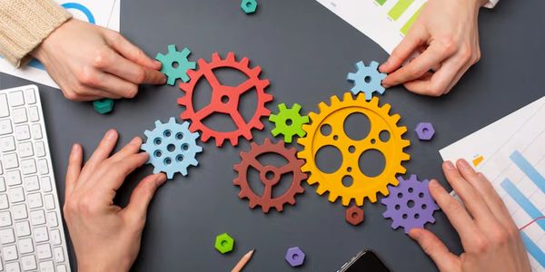 Hands assembling colorful wooden gears on a desk, symbolizing teamwork.