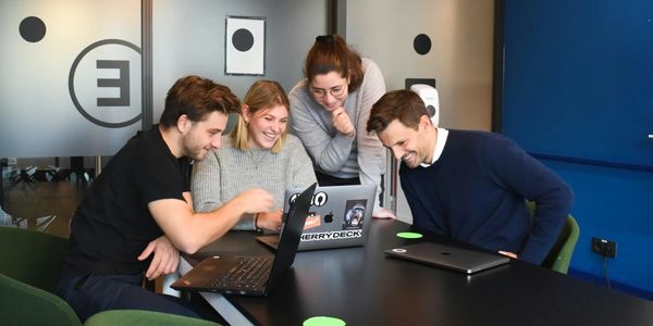 Four colleagues happily collaborating around laptops in a modern office.