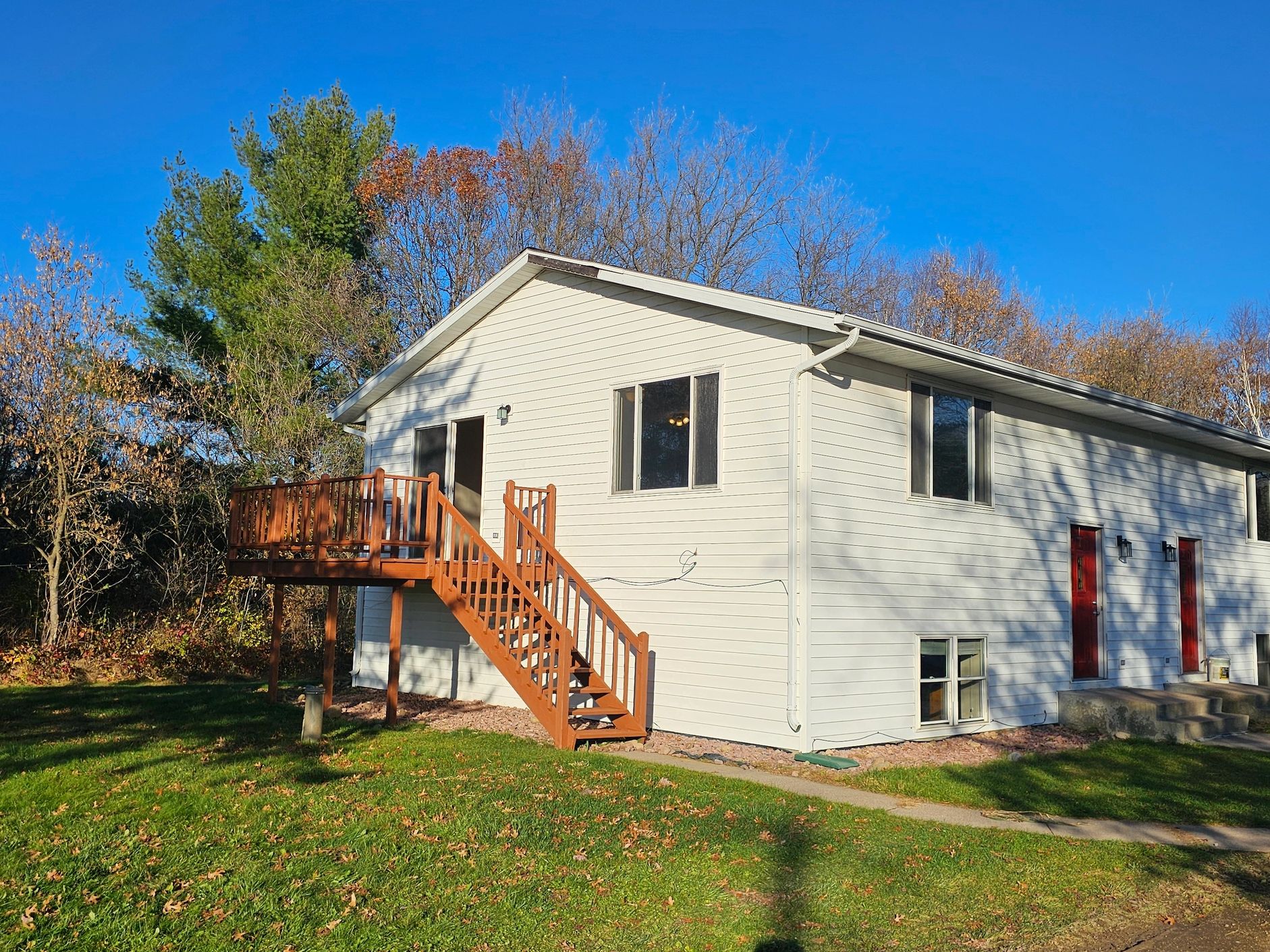 A white house with a wooden staircase and deck under clear blue skies.