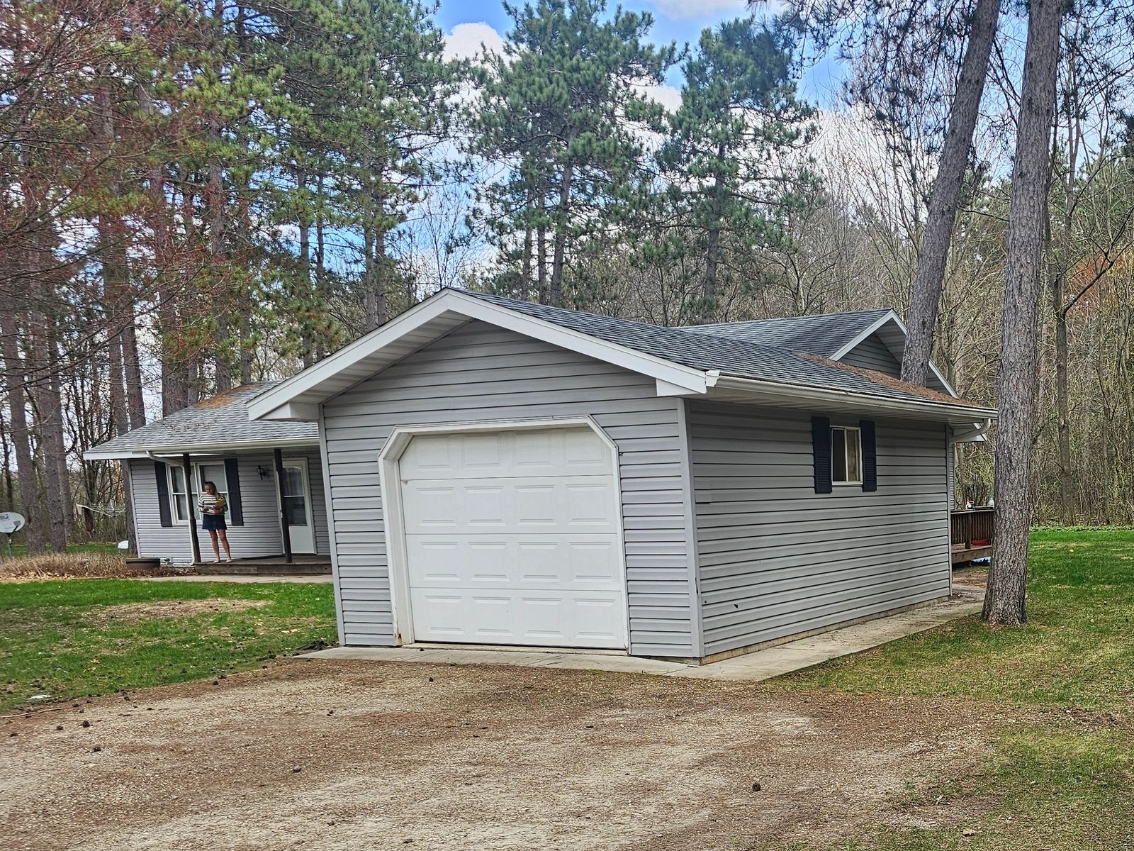 A gray detached garage and a house surrounded by trees on a sunny day.