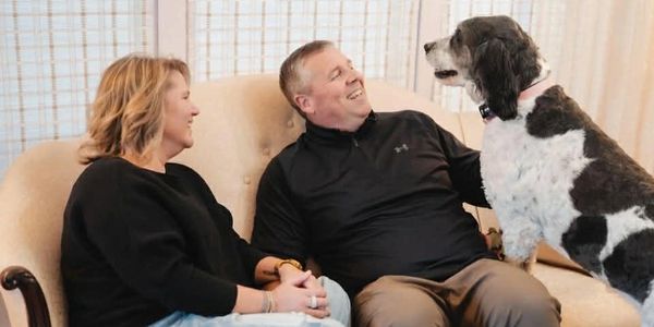 A couple joyfully interacting with their dog on a beige couch.