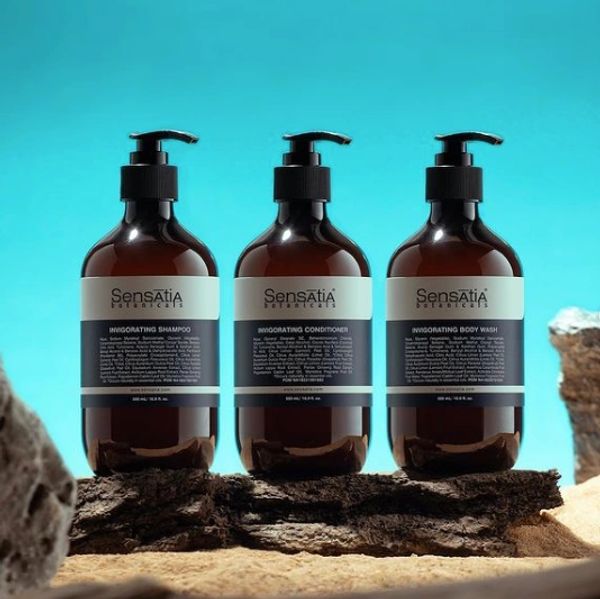 Three Sensatia Botanicals personal care bottles on a wooden surface with a blue background.