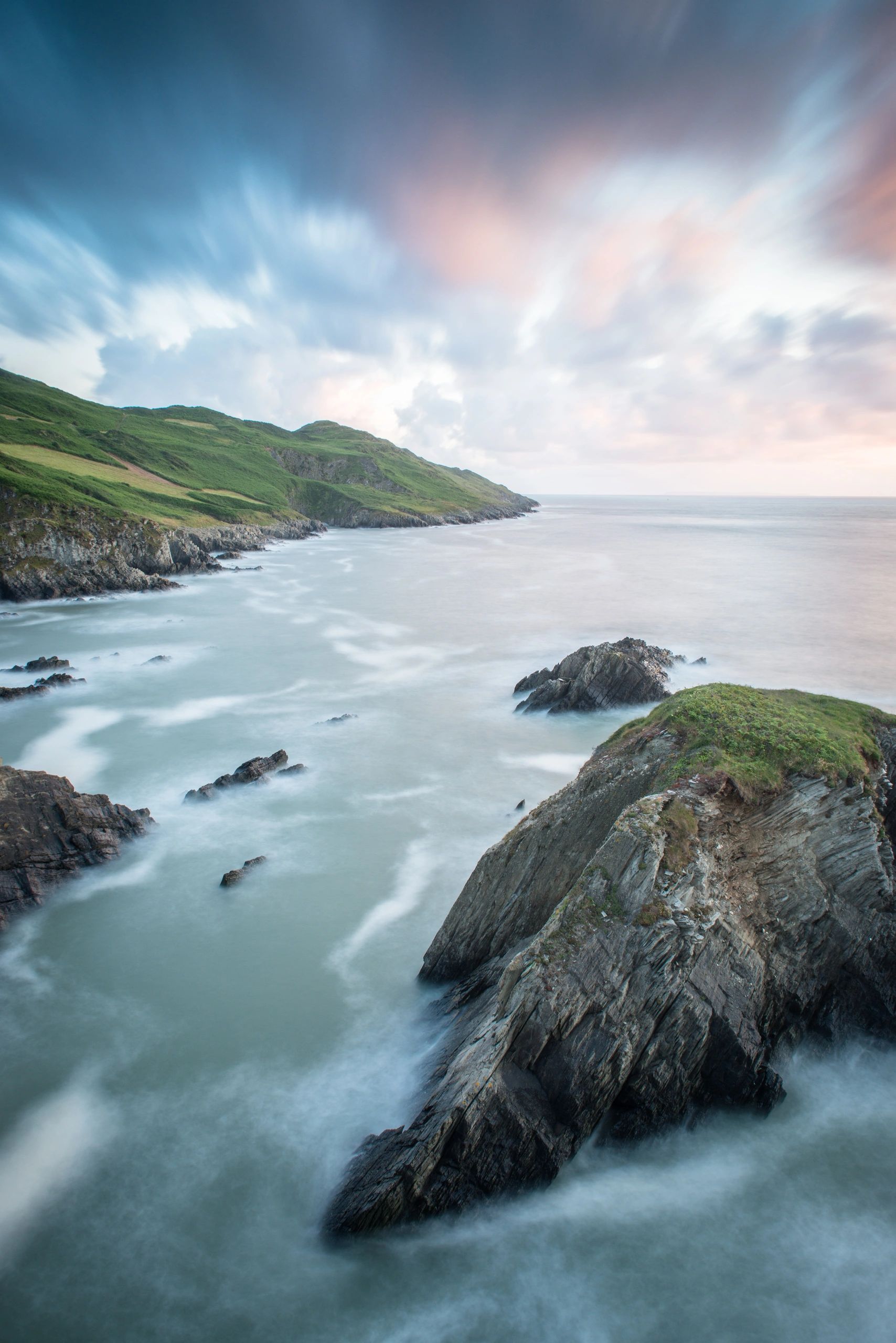 Misty ocean waves crash against rocky cliffs under a vibrant sky.