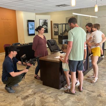 Family checks in at the reception desk while a photographer takes their photos from beside the desk.