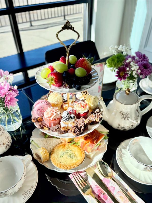 Three-tiered afternoon tea stand with fruits, desserts, and sandwiches on a table set for tea.