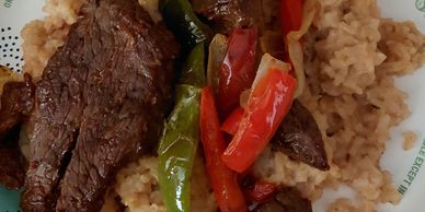 Grilled steak with sautéed bell peppers and rice on a white plate.