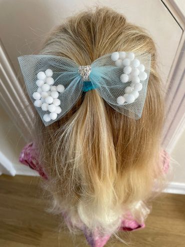 Photo of a blonde haired child with a pom pom bow hair bobble
