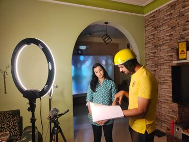 Man in yellow helmet explaining script to woman under ring light.